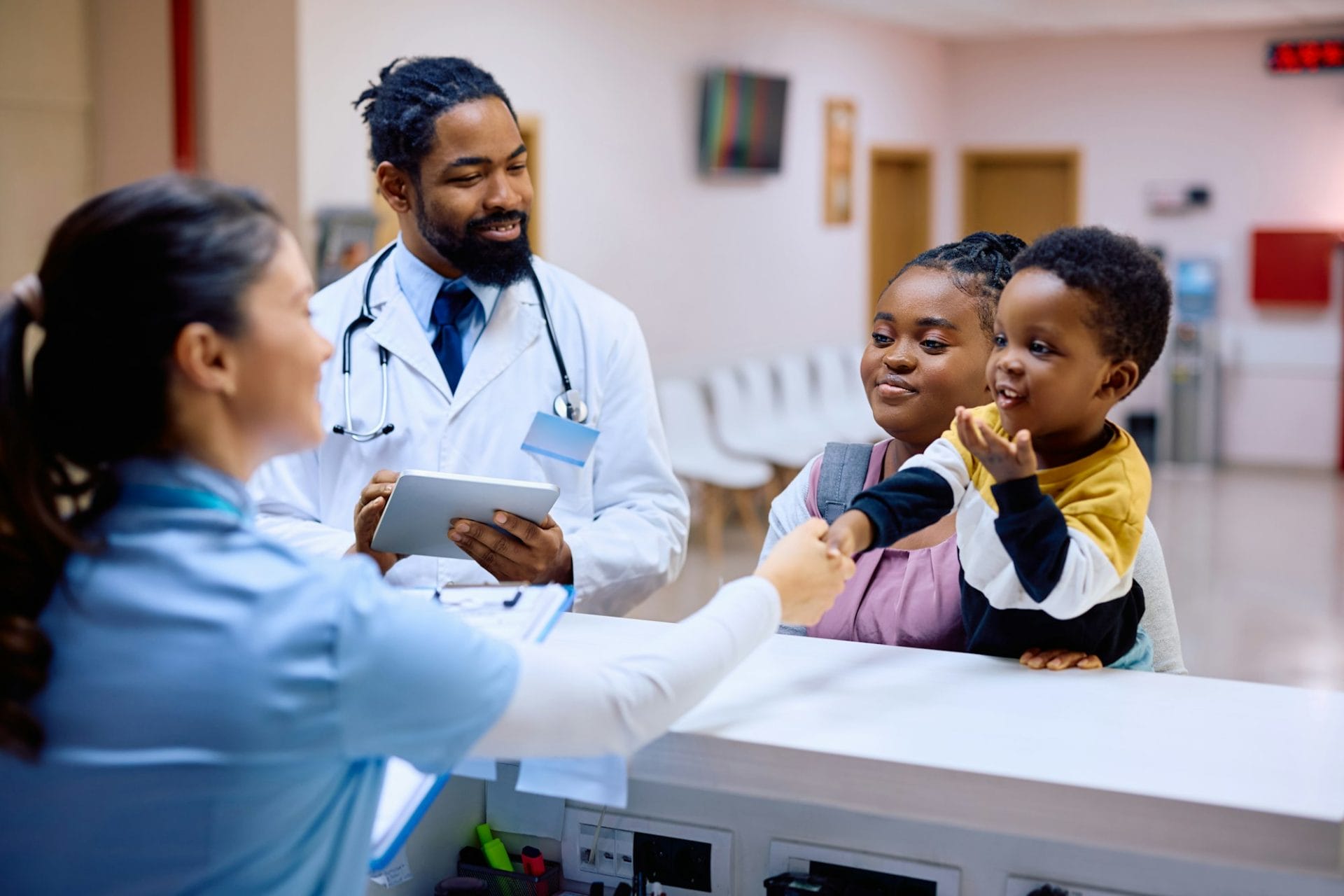 Happy black kid handshaking with reception nurse at pediatric clinic.