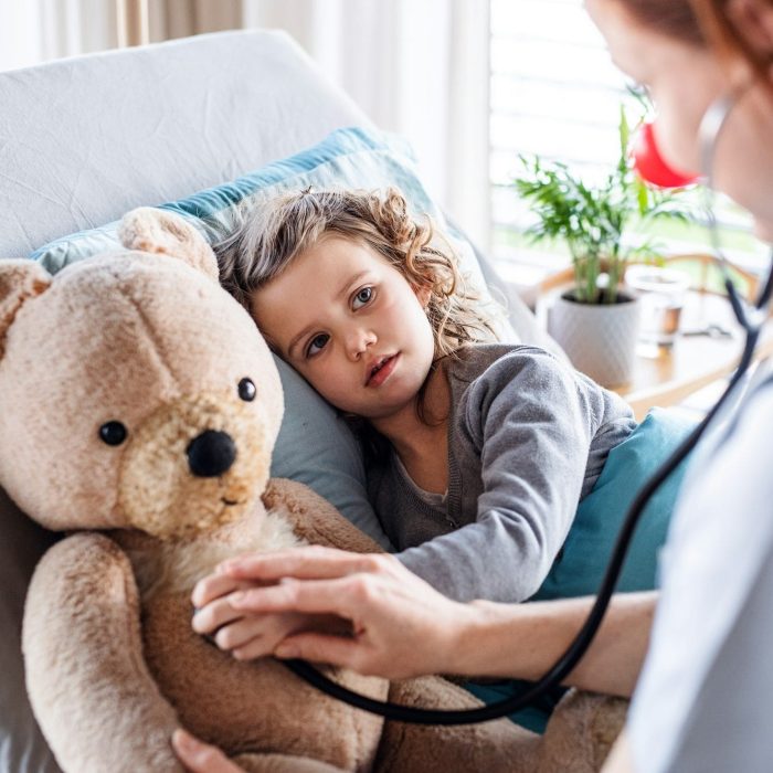 Friendly female doctor examining small girl in bed in hospital.