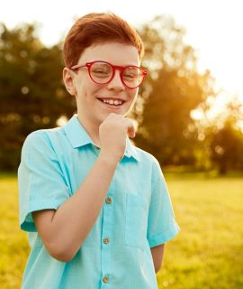 Happy kid in glasses standing on green meadow